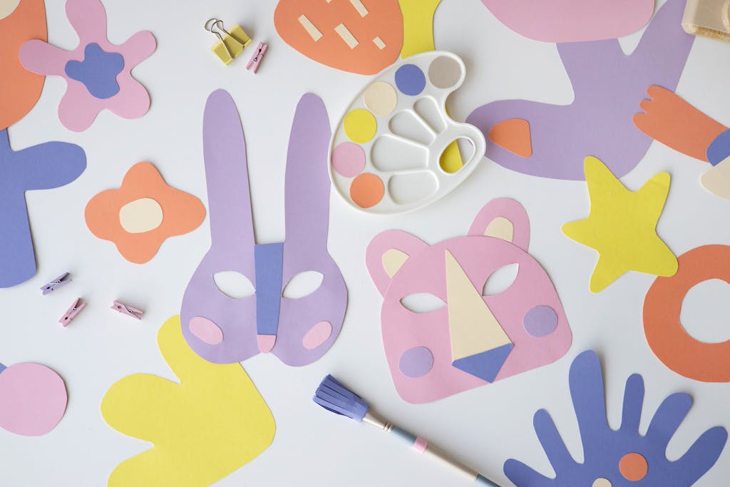 Creative flat lay of colorful paper masks and art materials on a white table.