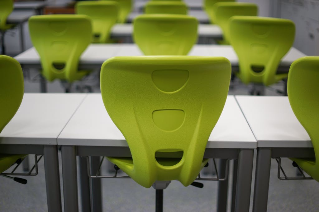 An empty modern classroom featuring rows of vibrant green plastic chairs and white desks.